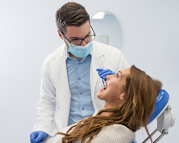 Implante Dentário Dói Entenda o Processo de Recuperação Sem Dor - Imagem Vista de alto ângulo do dentista examinando mulher com equipamentos odontológicos